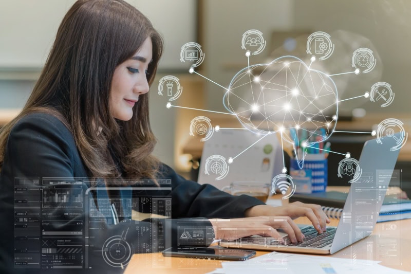 Asiatische Geschäftsfrau am Laptop vor digitalem Gehirn-Symbol für KI, mit Icons zu intelligenten Business-Technologien.