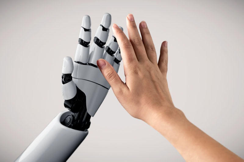 Roboterhand und Menschenhand beim High Five vor weißem Hintergrund.