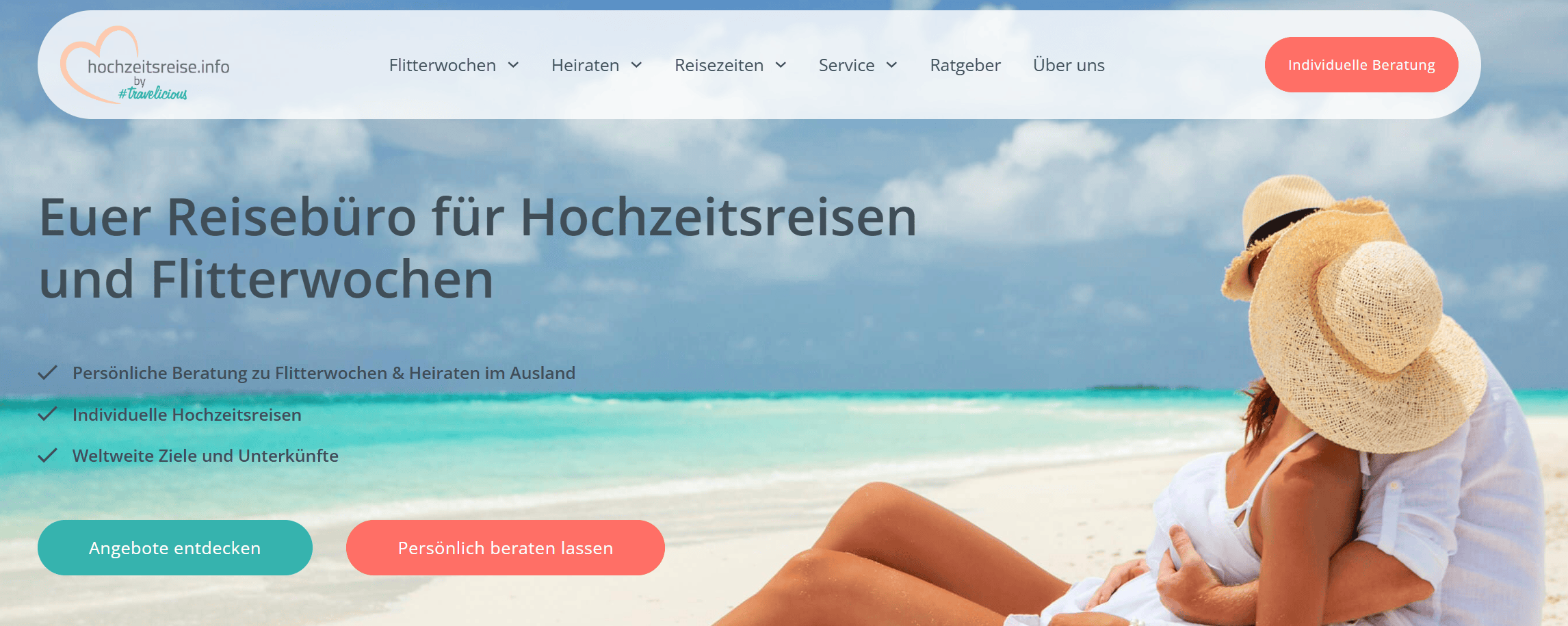 Paar mit Strohhüten umarmt sich am weißen Sandstrand mit türkisblauem Meer – Symbolbild für romantische Hochzeitsreisen und Flitterwochen.