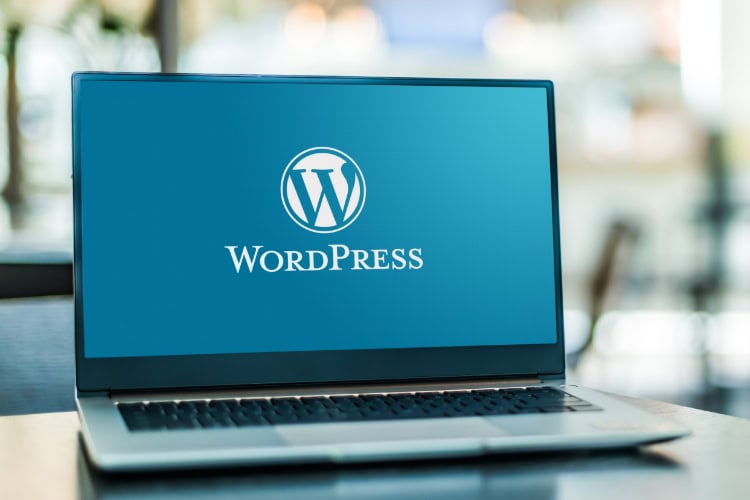 Ein geöffneter Laptop mit dem WordPress-Logo auf dem Bildschirm steht auf einem Tisch in einem modernen, hellen Raum